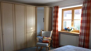Une chambre à coucher avec un lit, un fauteuil à bascule, une armoire et une fenêtre avec des rideaux.
