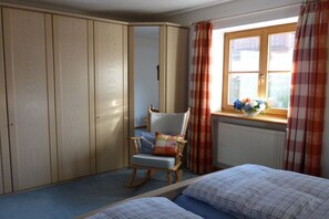 A bedroom with a bed, a rocking chair, a wardrobe, and a window with curtains. - Holiday apartment with 1 bedroom (Aschau\/Chiemgau)