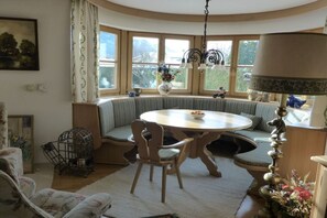 Ein gemütliches Zimmer mit einem runden Tisch, einer Bank und einem großen Fenster mit Vorhängen.
