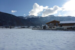A snow-covered landscape with a wooden building and mountains in the background. - Holiday apartment with 1 bedroom (Aschau\/Chiemgau)