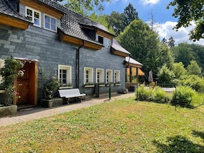 A two-story building with a grey exterior, a wooden door, and a bench outside. - Mühlenley - A secluded vacation home surrounded by nature, located above Monschau's Old Town (Monschau)