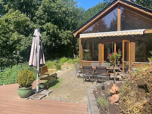 A wooden cabin with a covered patio area, outdoor seating, and a potted plant. - Mühlenley - A secluded vacation home surrounded by nature, located above Monschau's Old Town (Monschau)