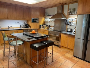 A kitchen with wooden cabinets, a stainless steel refrigerator, a microwave, and a stove. There are two bar stools and a large island with a pumpkin. - Mühlenley - A secluded vacation home surrounded by nature, located above Monschau's Old Town (Monschau)
