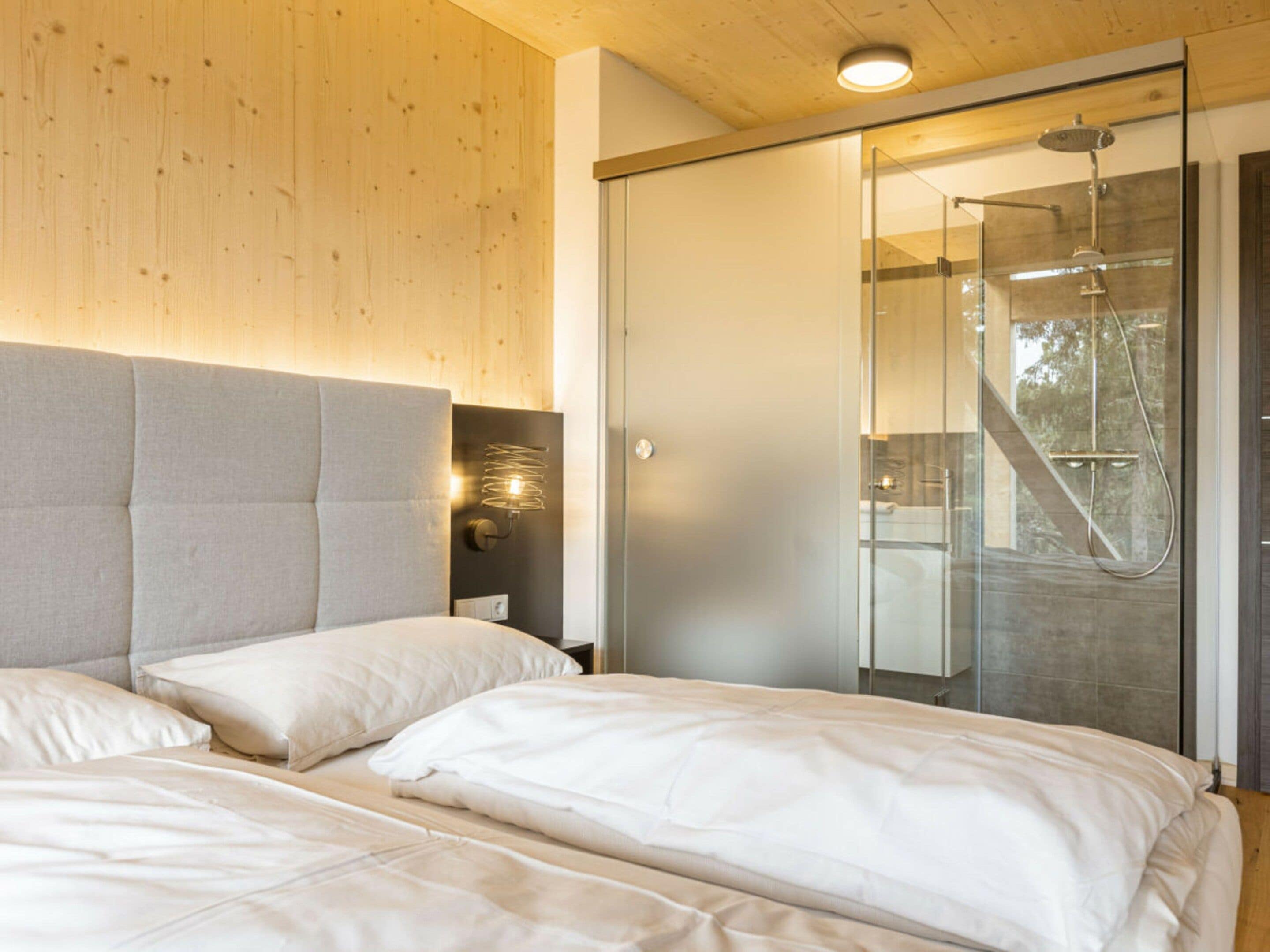 Une chambre moderne avec un grand lit, une douche en verre et un plafond en bois.