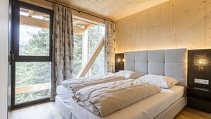A bedroom with a bed, curtains, a headboard, and a window with a view of trees. - Superior Chalet #16 With Sauna & Hot Tub (Stadl-Predlitz)