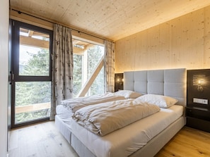 A bedroom with a bed, curtains, a headboard, and a window with a view of trees. - Superior Chalet #16 With Sauna & Hot Tub (Stadl-Predlitz)