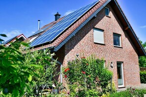 Ein Ziegelhaus mit Solaranlage auf dem Dach und einem Garten im Vordergrund.