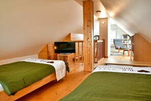 Ein Zimmer mit zwei Betten, einem Fernseher, Holzbalken und Blick auf einen Balkon.