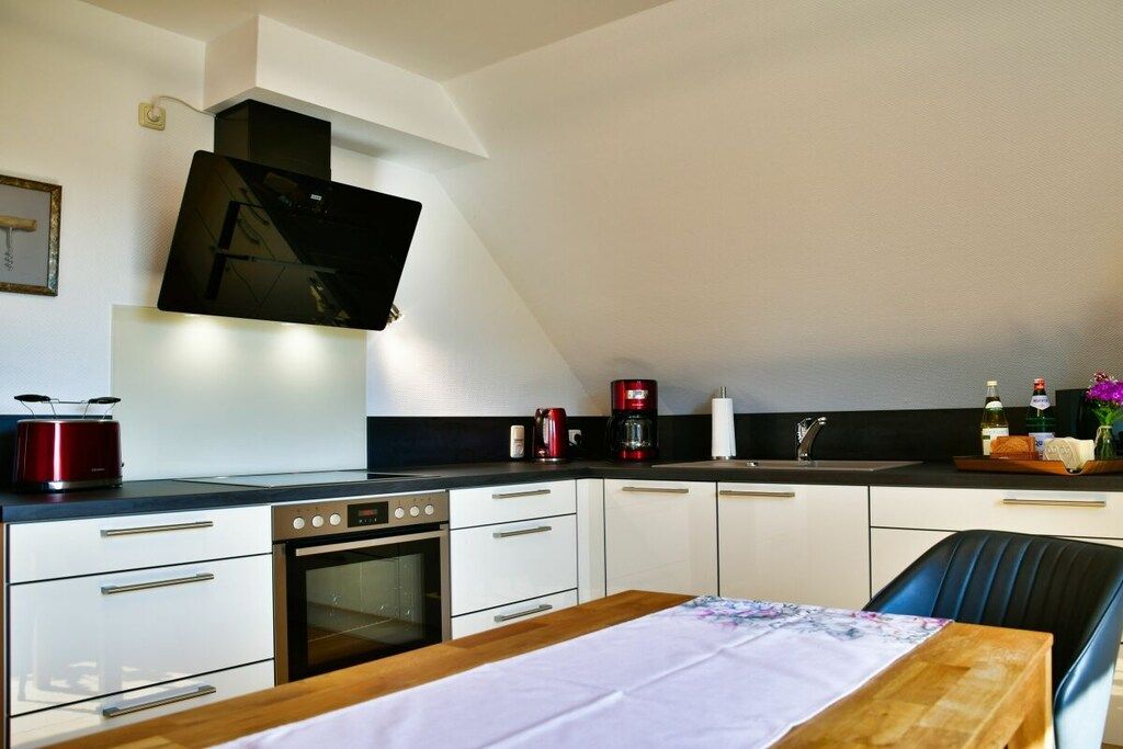 Una cocina moderna con un televisor de pantalla plana, un hervidor rojo, una cafetera y una mesa de comedor de madera.