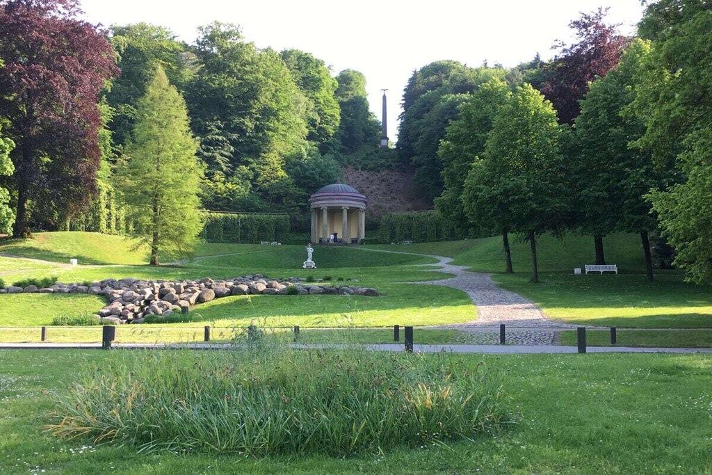 A landscaped garden with a central gazebo, a winding path, and a statue.