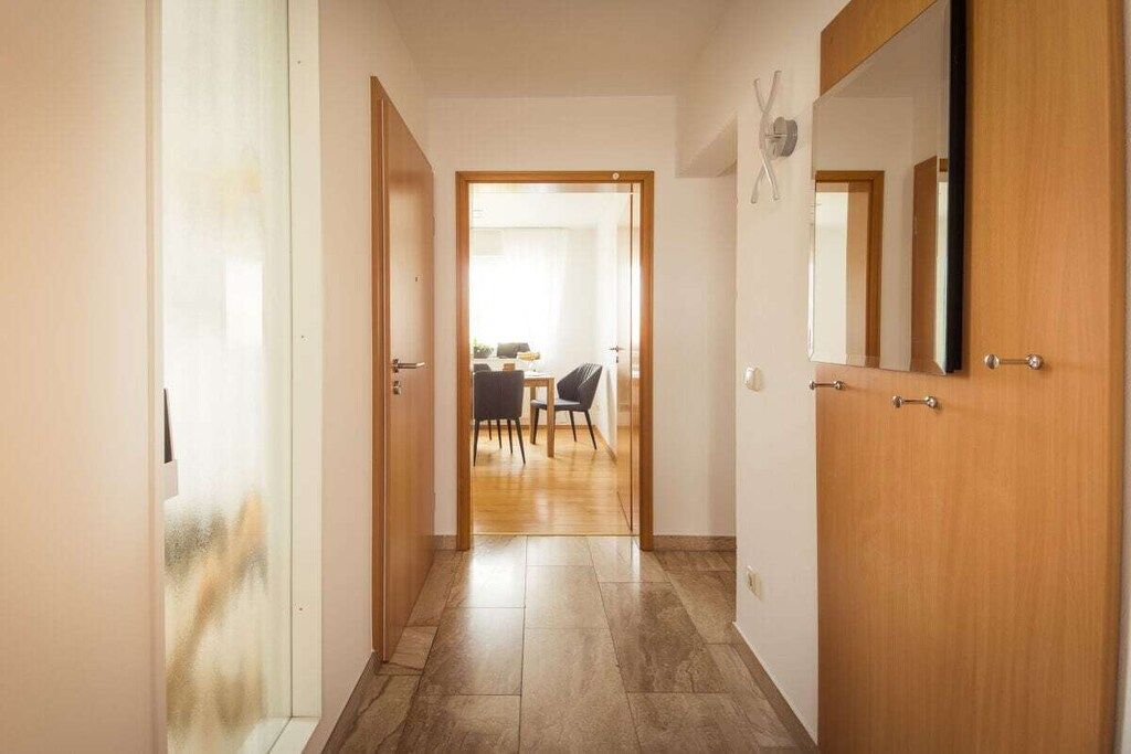 Ein Flur mit einer Holztür rechts, einer weißen Tür links und Blick in einen Essbereich mit Tisch und Stühlen.