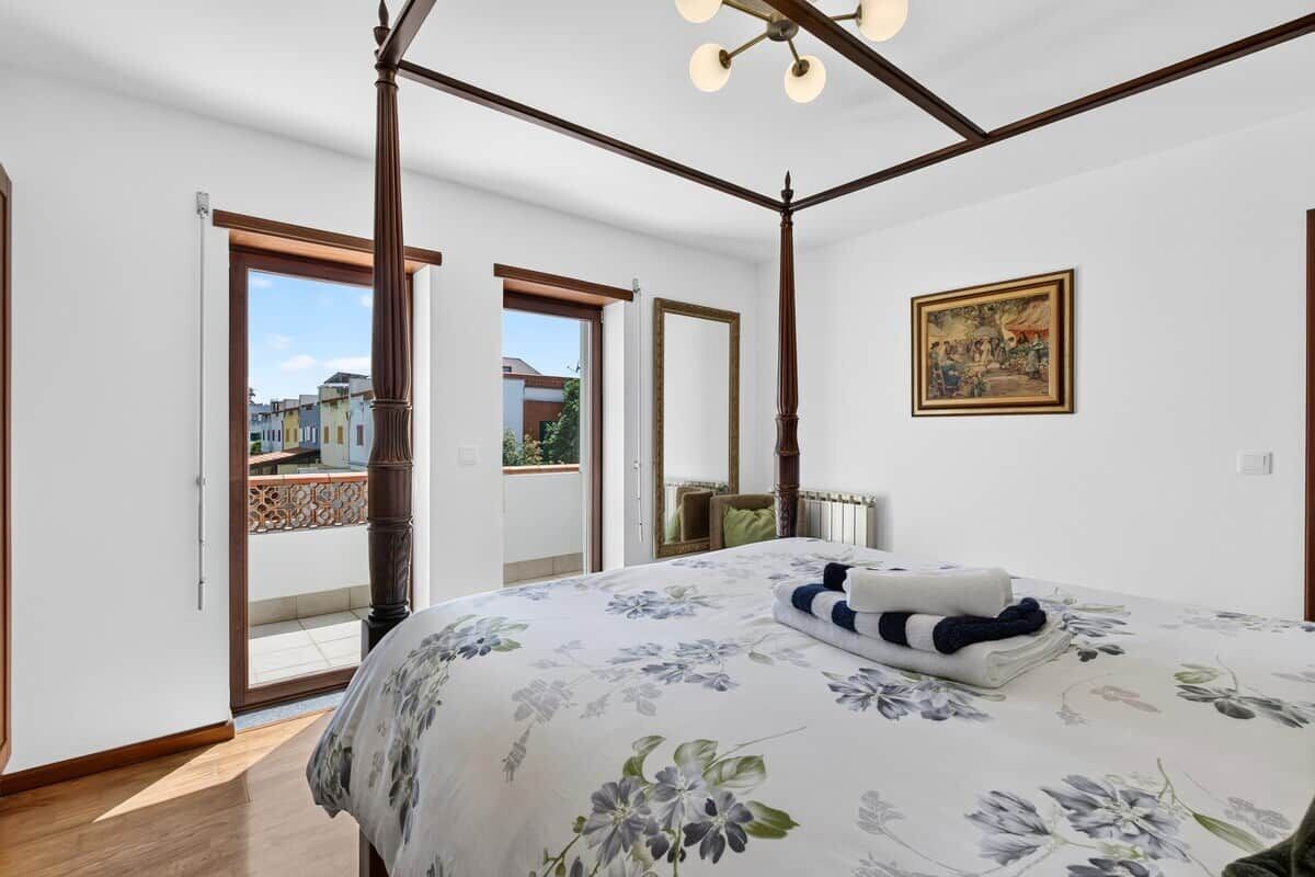 A bedroom with a large bed, a ceiling fan, a window, and a door leading to a balcony.