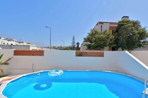 A swimming pool with a clear blue water surface, surrounded by a white wall with decorative tiles, and a tree to the right. - Lagosta Beach House (Gafanha da Boa Hora)