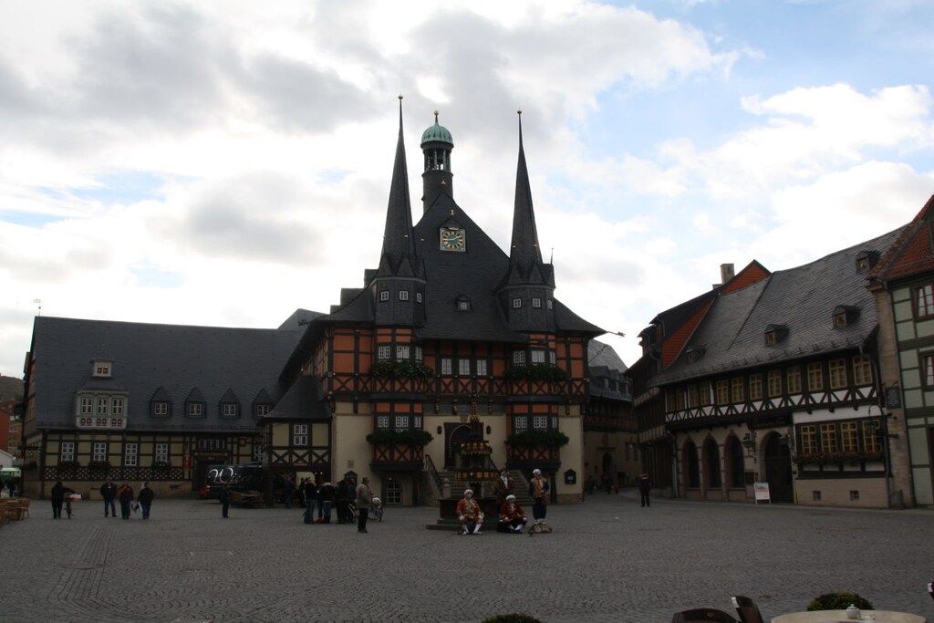 Un edificio histórico con una torre de reloj, fachadas tradicionales con entramado de madera y un patio adoquinado.