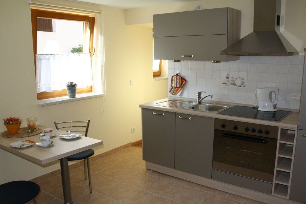 A compact kitchen with a dining area, a window with curtains, and a built-in oven.