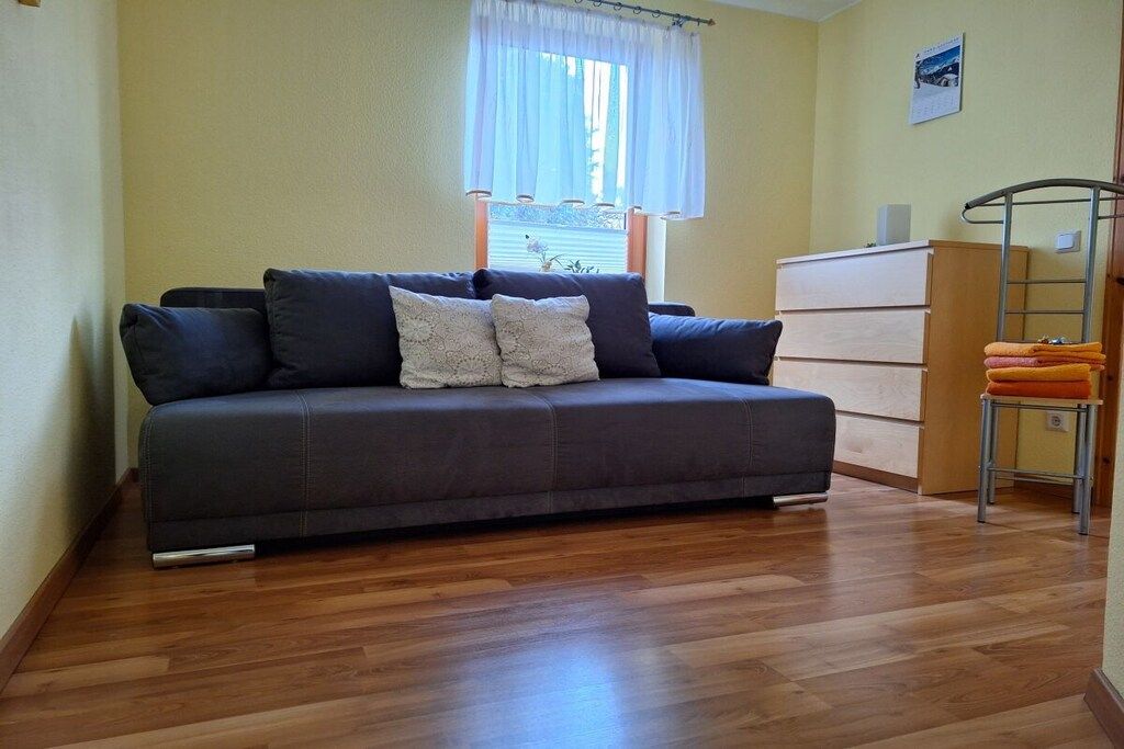 Een kamer met een bank, een houten dressoir en een raam met gordijnen.