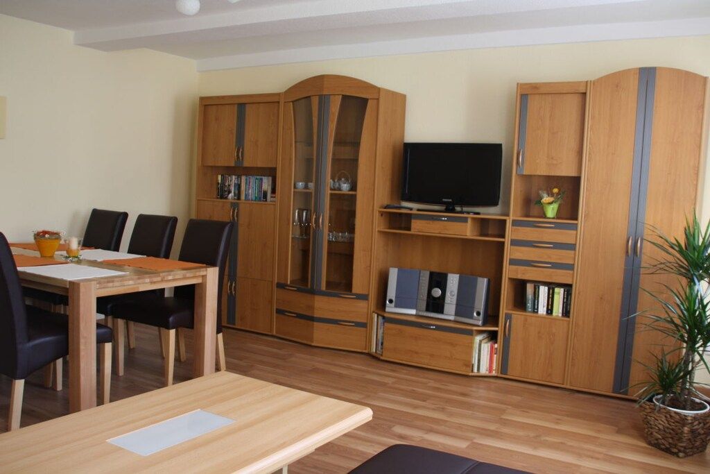A living room with a wooden dining table, chairs, a TV, and built-in wooden cabinets with shelves.