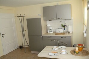 A compact kitchen with a white door, grey cabinets, a coffee maker, and a table set with plates and cups. - Holiday apartment with 2 bedrooms (Wernigerode)