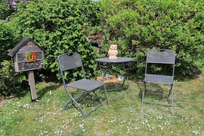 A garden with two metal chairs, a birdhouse, and a decorative owl statue. - Holiday apartment with 2 bedrooms (Wernigerode)