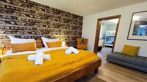 A bedroom with a brick-patterned headboard, a bed with white and yellow bedding, a wooden bench, and a grey sofa. - Bergstadthaus Sankt Andreasberg (St. Andreasberg)