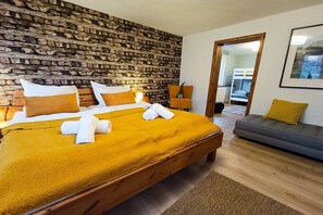 A bedroom with a brick-patterned headboard, a bed with white and yellow bedding, a wooden bench, and a grey sofa. - Bergstadthaus Sankt Andreasberg (St. Andreasberg)