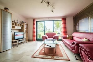 A living room with a red sofa, a glass coffee table, a television, and a sliding glass door leading to an outdoor area. - Holiday home with 1 bedroom (Boltenhagen OT Redewisch)