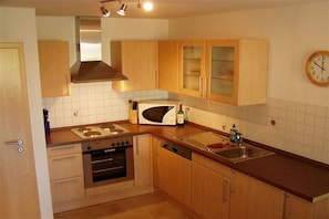 A compact kitchen with wooden cabinets, a microwave, a stove, and a sink. - Holiday home with 1 bedroom (Boltenhagen OT Redewisch)