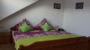 Een slaapkamer met een schuine kap, een houten bed, twee nachtkastjes, een lamp en twee aan de muur bevestigde foto's.