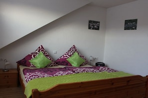 Camera da letto con soffitto spiovente, un letto in legno, due comodini, una lampada e due quadri appesi al muro.