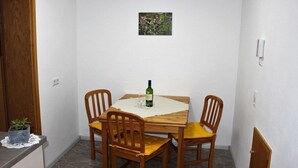 Een gezellig eetgedeelte met een houten tafel, vier stoelen, een fles wijn en een kleine plant op het aanrecht.