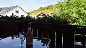 Een tafel met een fles en twee glazen op een balkon met uitzicht op een woonwijk met huizen en groen.