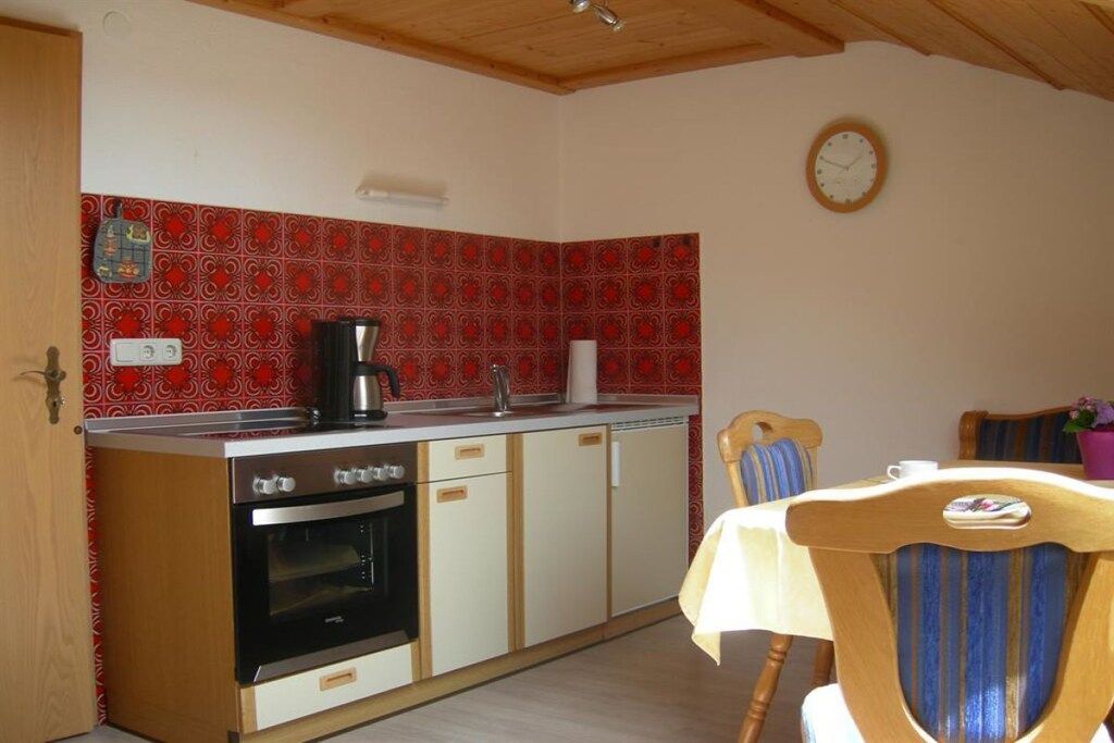 A kitchen with a stove, oven, and coffee maker. There is a dining table with chairs and a clock on the wall.