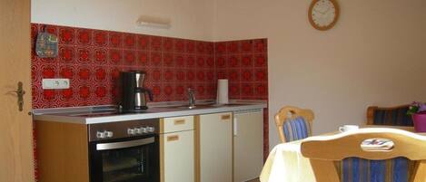A kitchen with a stove, oven, and coffee maker. There is a dining table with chairs and a clock on the wall.