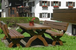 A wooden picnic table with benches, surrounded by a well-maintained garden with flowers and a hedge. - Holiday apartment with 1 bedroom (Sonthofen)
