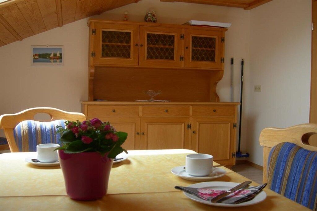 Un coin repas avec une table dressée pour deux personnes, une plante en pot et des meubles en bois en arrière-plan.