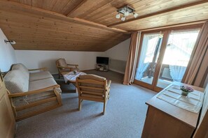 Ein gemütliches Dachzimmer mit schrägen Wänden, Holzmöbeln, einem Fernseher und Blick durch eine Glastür.