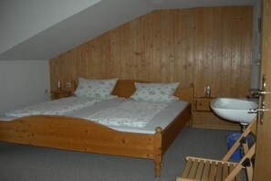 A bedroom with a wooden sloped ceiling, a wooden bed with floral bedding, a bedside table, and a wooden chair. - Holiday apartment with 1 bedroom (Sonthofen)
