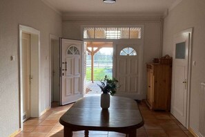 Ein Flur mit einem Holztisch, einer Topfpflanze und Blick ins Freie durch eine Tür.