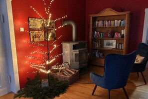Een kamer met een open haard, een boekenkast, een blauwe stoel en een kerstboom met lichtjes.