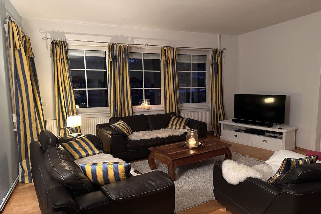 Ein Wohnzimmer mit einem schwarzen Ledersofa, einem Holztisch und einem Fernseher auf einem weißen Lowboard.