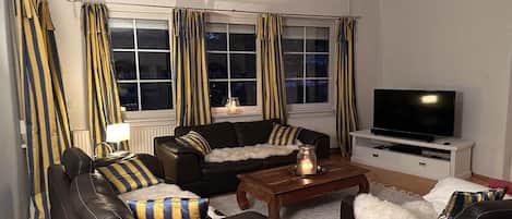 Ein Wohnzimmer mit einem schwarzen Ledersofa, einem Holztisch und einem Fernseher auf einem weißen Lowboard.