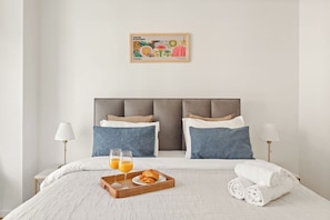A hotel room with a bed, pillows, a tray with croissants and orange juice, and a framed artwork on the wall. - Charming 2BR in Saint-Germain-des-Pres (Paris)