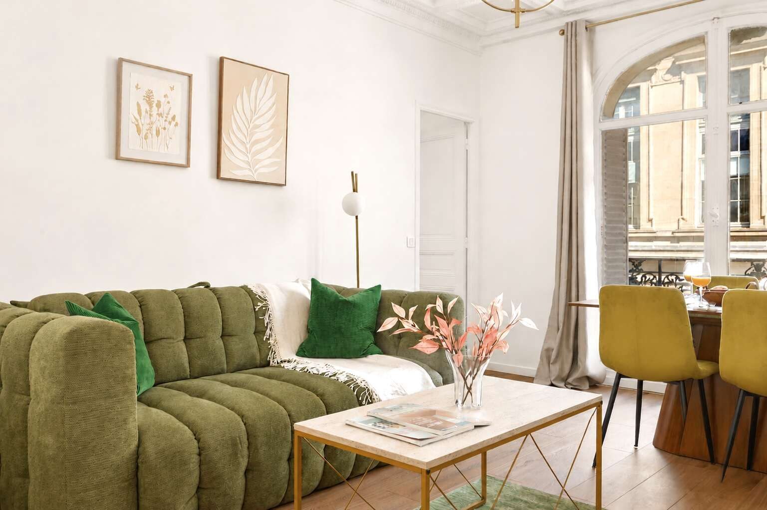 Un salon avec un canapé vert, une table basse et un coin repas avec des chaises jaunes.