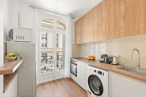 A compact kitchen with a washing machine, a sink, and a small window overlooking a balcony. - Charming 2BR in Saint-Germain-des-Pres (Paris)