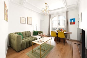 A living room with a green sofa, yellow chairs, a dining table, and a chandelier. - Charming 2BR in Saint-Germain-des-Pres (Paris)