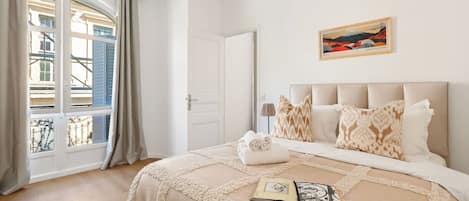 Une chambre d’hôtel avec un grand lit, une vue sur les immeubles par la fenêtre et un tableau accroché au mur.