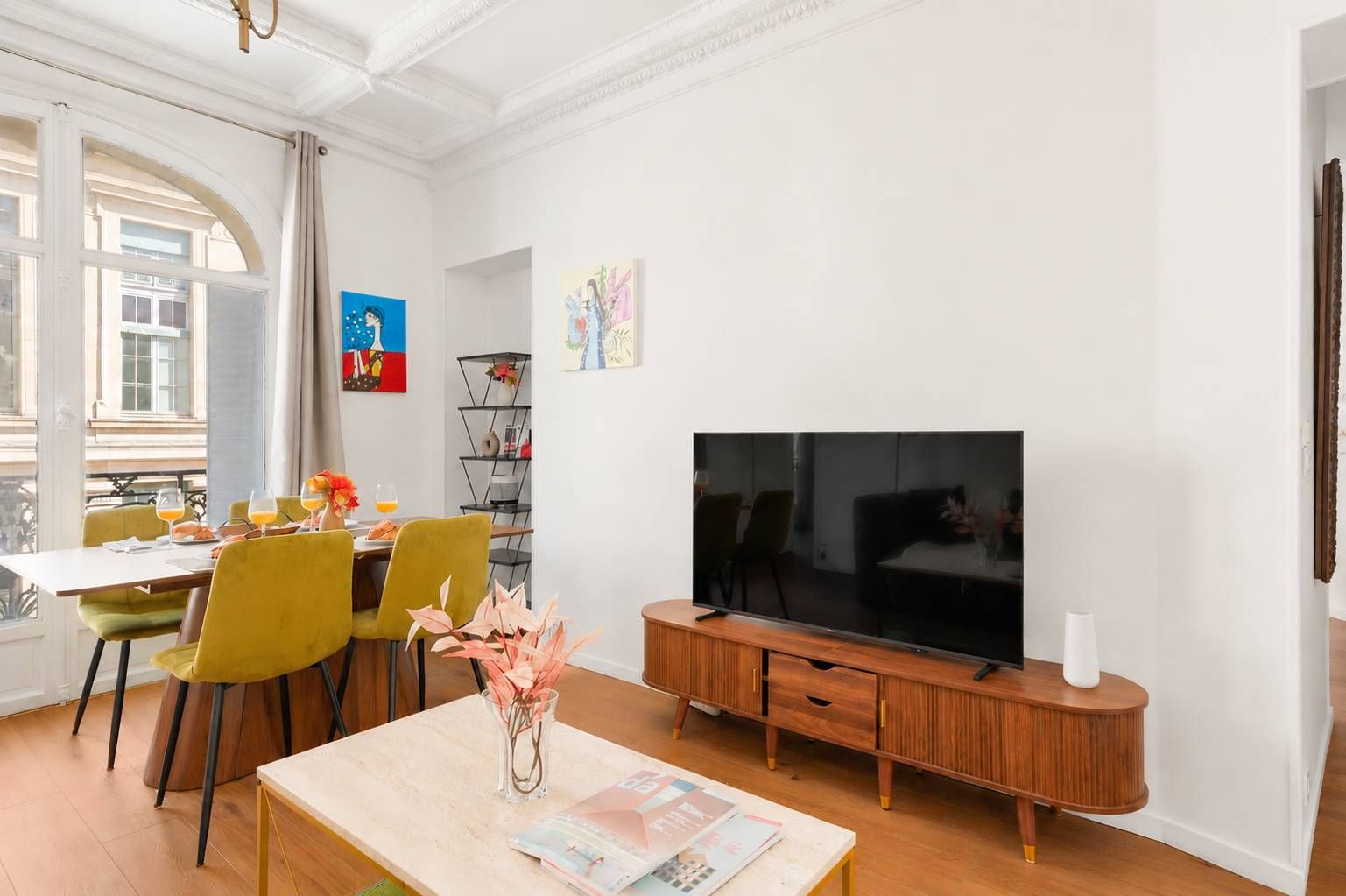 Een woonkamer met een televisie, een eettafel met stoelen en een boekenkast.