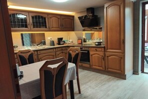 Une cuisine avec des meubles de rangement en bois, une table à manger avec des chaises et un four encastré.