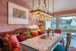 A dining area with a wooden bench, a table with a floral tablecloth, and a chandelier. - Holiday apartment House of the Painters' Cloud Two (Müllheim)