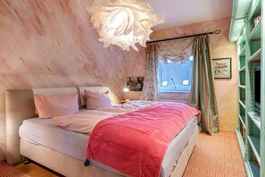 A bedroom with a bed, a nightstand, a lamp, a window with curtains, and a bookshelf. - Holiday apartment House of the Painters' Cloud Two (Müllheim)